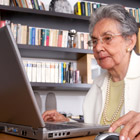 Elderly woman sitting at a laptop.
